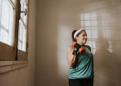 Senior woman in a brightly lit room exercises with dumbbells, promoting fitness at home.