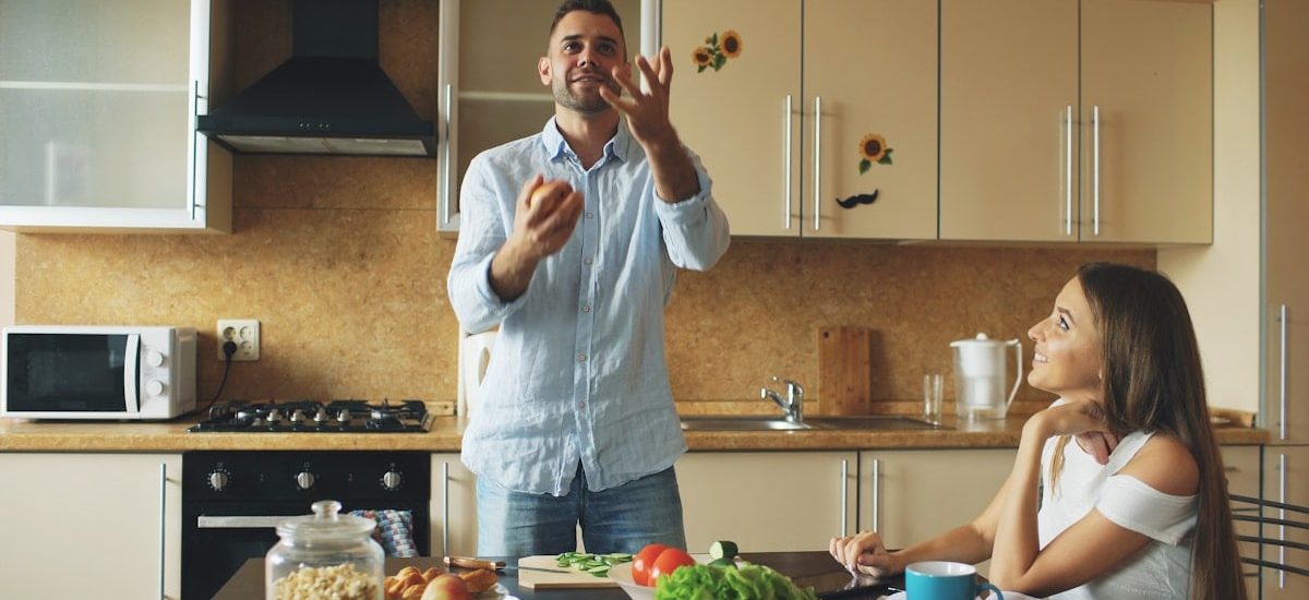 Attractive loving couple having fun in the kitchen. Handsome man juggle with apples to impress his girlfriend at home