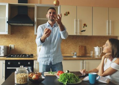 Attractive loving couple having fun in the kitchen. Handsome man juggle with apples to impress his girlfriend at home